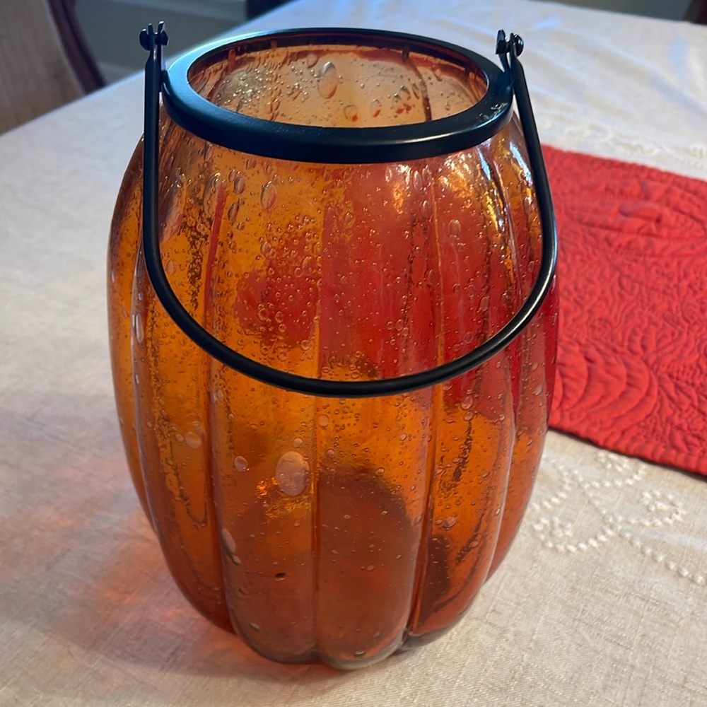 Orange oblong bubbled-glass pumpkin with black handle.